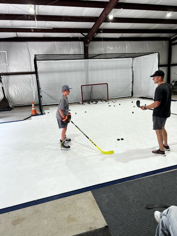 Hockey player executing a slap shot on Skate Anytime Synthetic Ice in a training center."