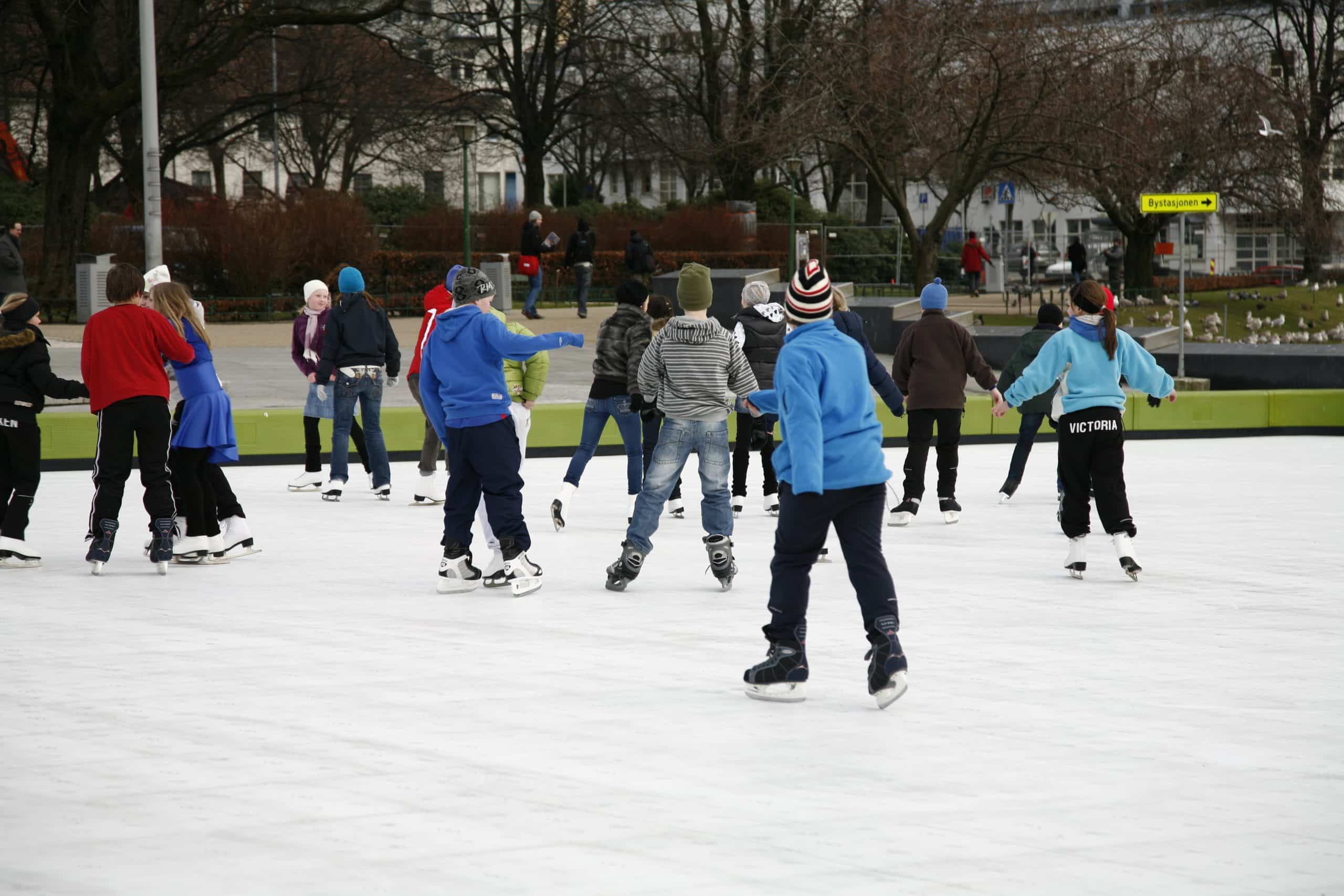 Community members skate under the lights in the town square. Evening skating on a well-lit synthetic ice rink in a town square